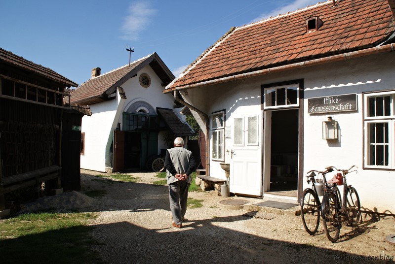 Dorfmuseum Mönchhof älterer Herr spaziert an Milchhaus und Wagnerei vorbei