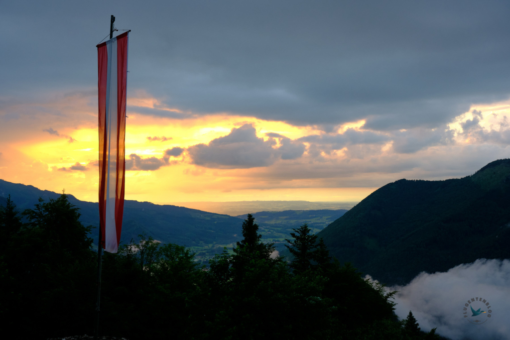vorne links die österreichische Flagge, hinten Abendstimmung und Blick ins Tal
