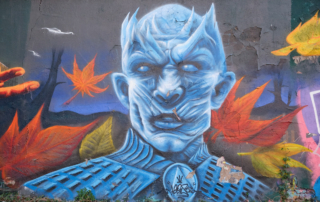 eisblauer Mann mit stechend blauen Augen und Hörnern auf dem Kopf, im Hintegrund fallendes Herbstlaub